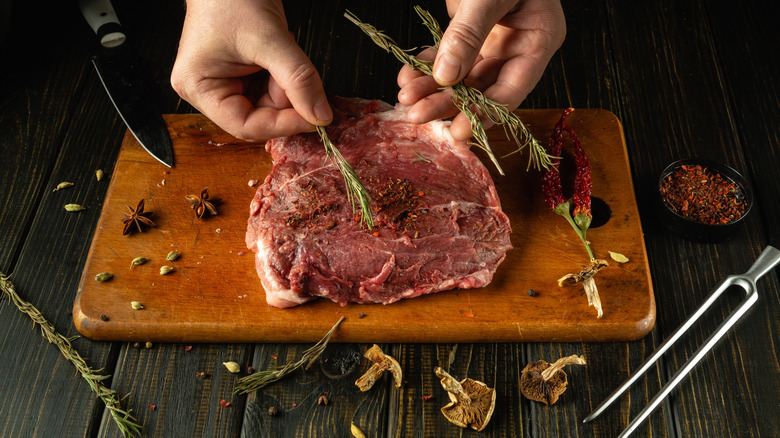 A person adding aromatics to a piece of meat on a cutting board