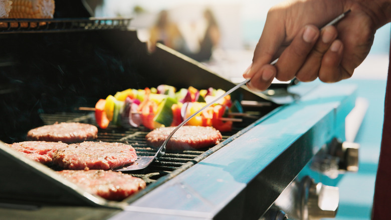 Closeup of a person flipping a hamburger on a grill at a barbecue.