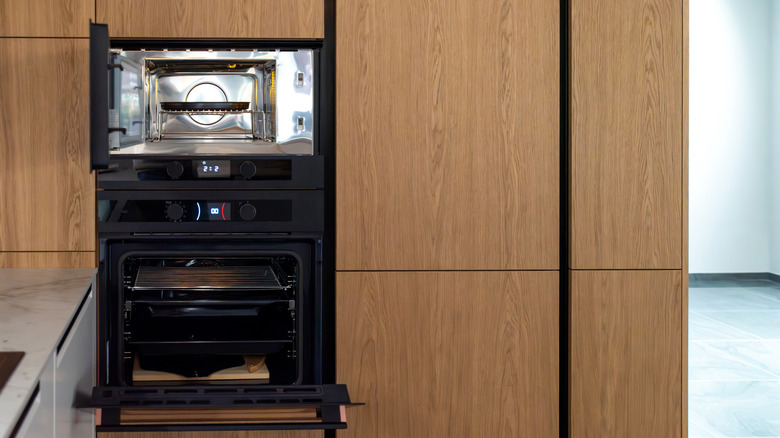 A double oven with the top door open, set in wood cabinets