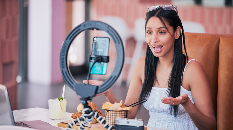 Female influencer using a tripod, a ring light, and a phone to record herself and her meal