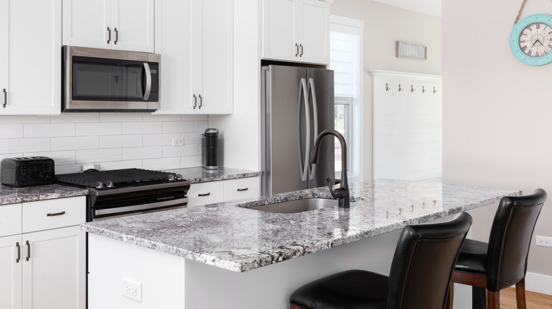 Leathered granite countertop with chairs in white kitchen