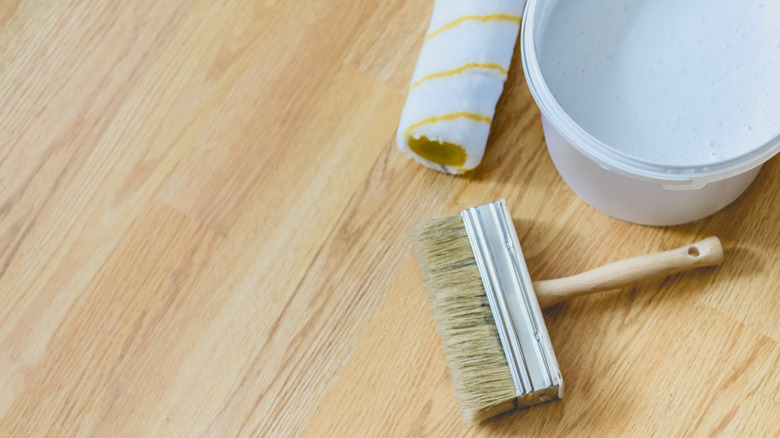 A bucket of paint, paint brush and roller on laminate