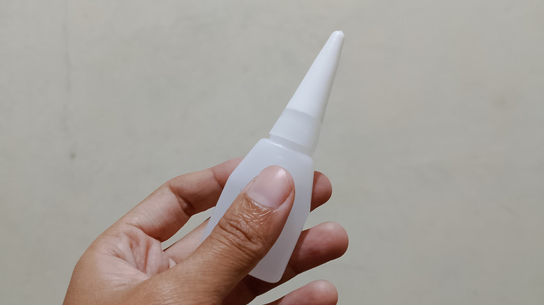 A hand holding a small bottle of super glue