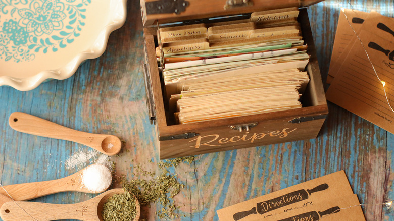 A box of vintage recipes beside spoons filled with spices