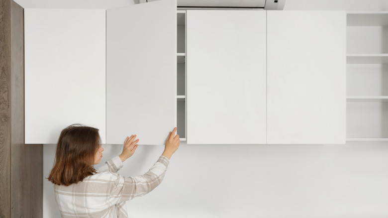 A woman opening a set of white kitchen cupboards