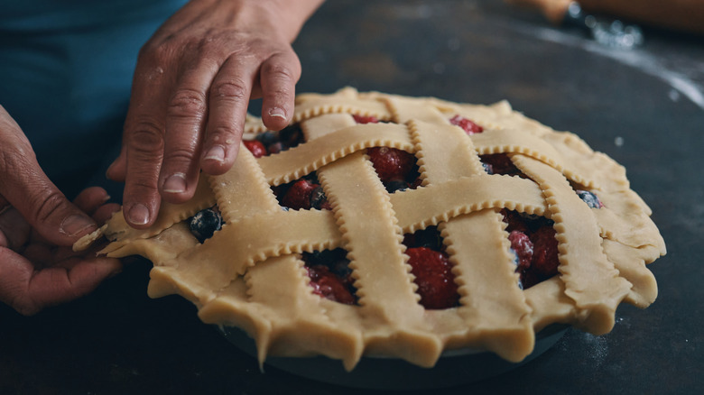Hands putting the top of the raw pie crust onto the filling