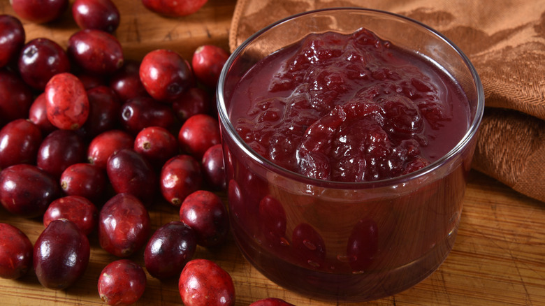 a small glass bowl of cranberry sauce on a wooden table with whole cranberries