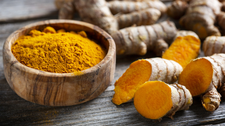 View of ground turmeric in a bowl alongside fresh turmeric on a table