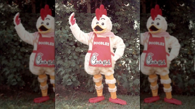 Doodles the chicken mascot in a red apron waving at the camera