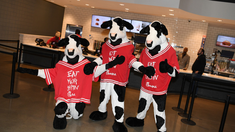 Chick-fil-A cow mascots standing in front of a Chick-fil-A restaurant
