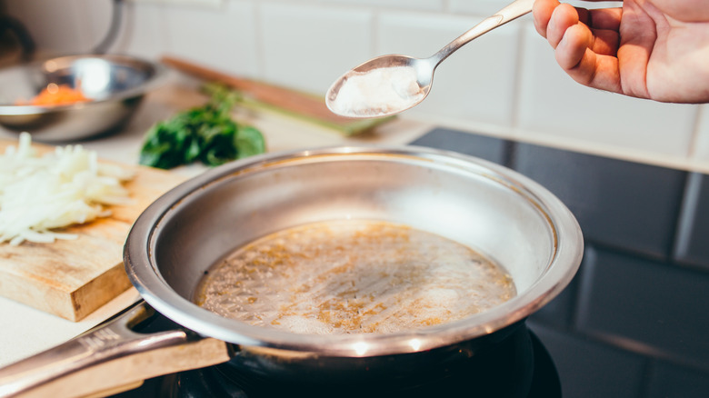 Someone pouring a spoon of baking soda into water and vinegar in a pan with calcium deposits