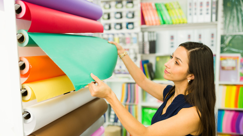 A woman pulling out green contact paper from a roll in a shop