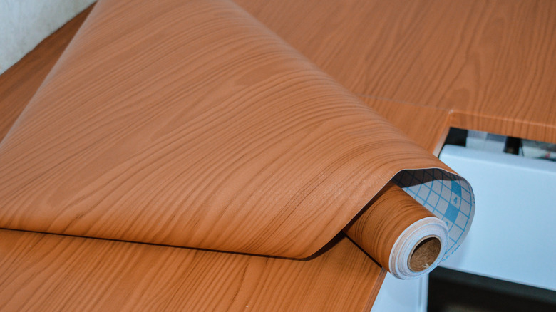 A roll of faux-wood style contact paper on a kitchen counter that has been remodeled using the paper
