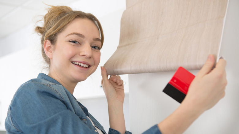 A smiling woman holding a sheet of adhesive vinyl as she installs it in the kitchen