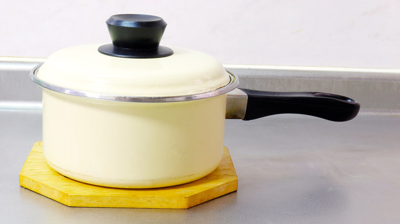 A white saucepan with a lid placed on a yellow trivet on a kitchen counter