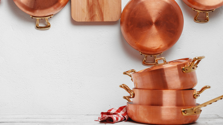 Copper pots stacked on table in front of hanging copper pans