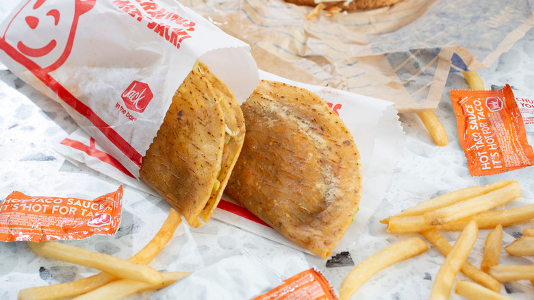 Two Jack in the Box tacos in a wrapper beside fries
