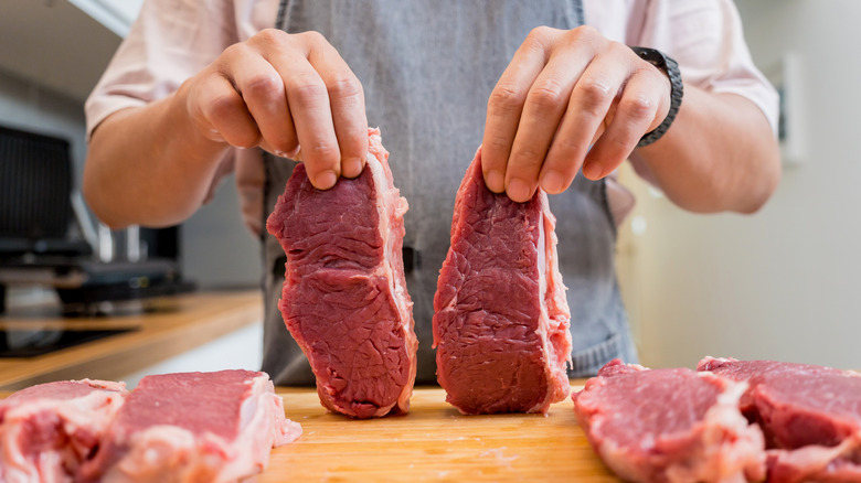 A man holding up two raw cuts of beef