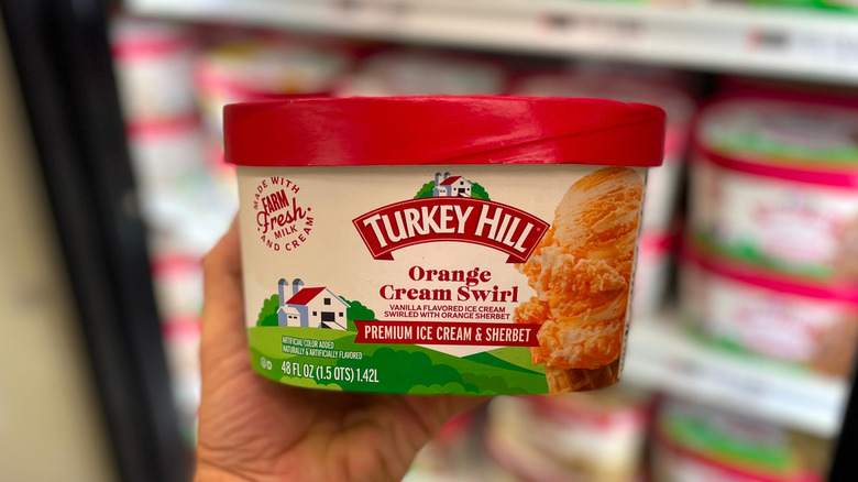 A hand holding a container of Turkey Hill Orange Cream Swirl