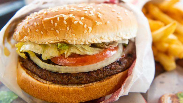 Close up of a hamburger topped with lettuce, tomato, and visible onion on a sesame seed bun