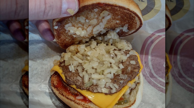 A close up of a hand lifting the top bun off a McDonald's cheeseburger to show an abundance of small, finely diced onions.