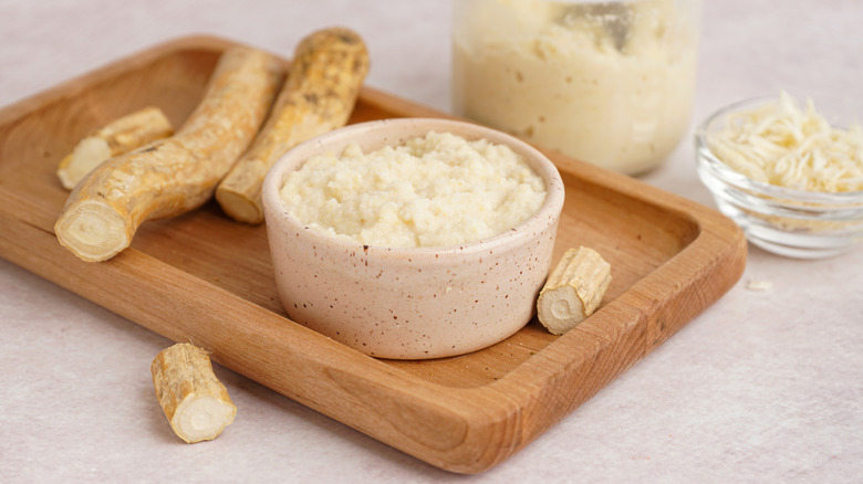 Horseradish sauce in a small glass dish surrounded by horseradish root