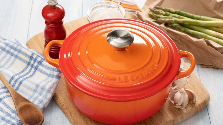 orange Le Creuset Dutch oven with cooking utensils and asparagus