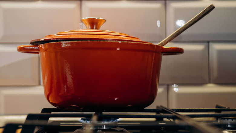 orange Dutch oven sits on gas stove with wooden utensil