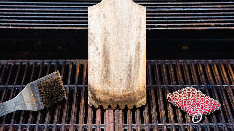 A rusted gas grill grate with various grill cleaning items.