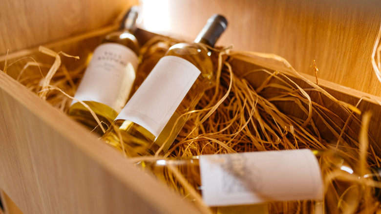 Three bottles of white wine resting in a crate filled with straw
