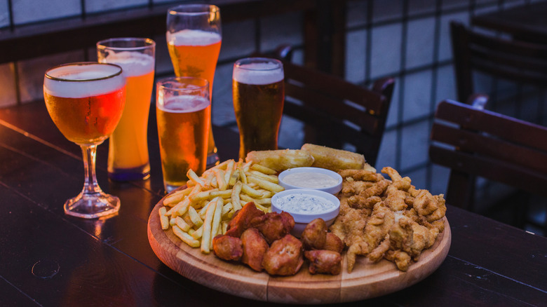 A platter of pub food included French fries and chicken wings, sitting next to several glasses of beer
