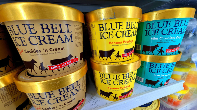 Tubs of Cookies n' Cream, Banana Pudding, and Mint Chocolate Chip Blue Bell ice cream stacked on a shelf.