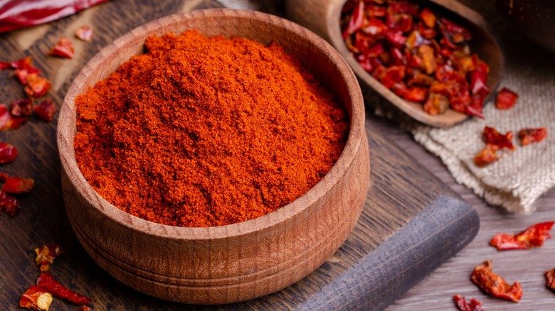 Close-up of cayenne powder in a wooden bowl next to dried red peppers