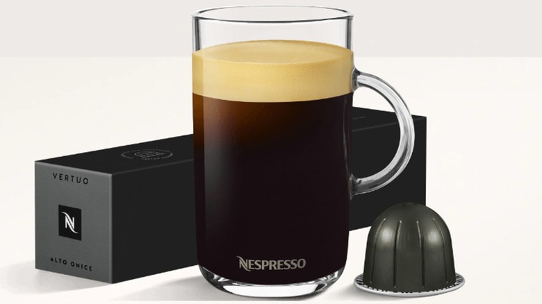 A Nespresso XL pod next to a cup of coffee and a box of pods