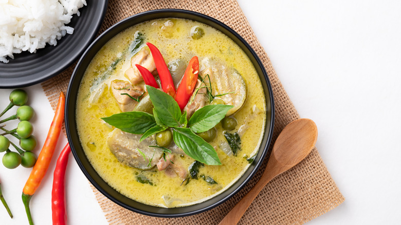 a bowl of Thai green curry topped with chiles and Thai basil, with rice and chiles around it