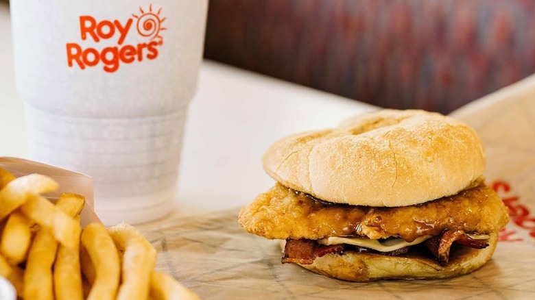 A Roy Rogers Gold Rush Chicken Sandwich on a wrapper next to fries and a drink