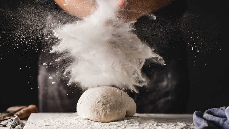 person throwing flour on dough