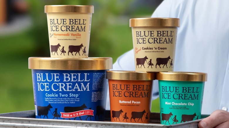 Person holding tray of various Blue Bell ice cream containers outside