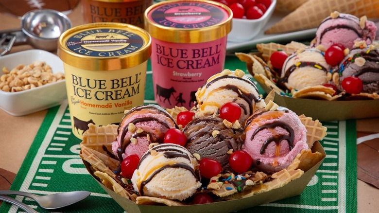Ice cream sundae with waffle cone pieces next to two Blue Bell pints