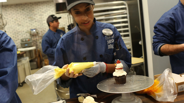 baker decorating a cupcake at a grocery bakery