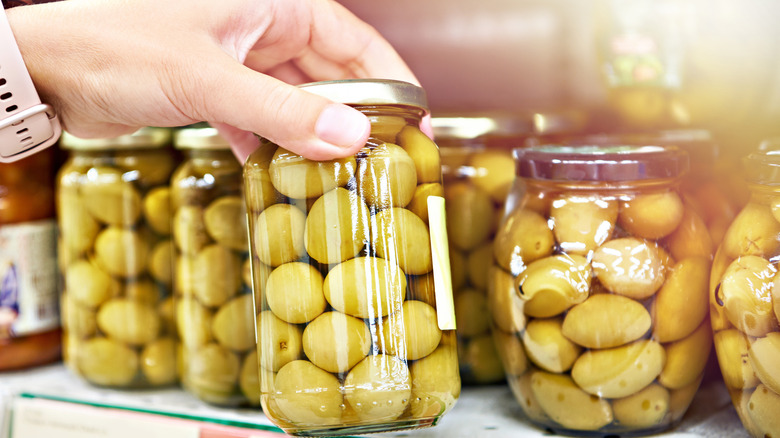 Woman selecting a jar of green olives from a grocery store shelf