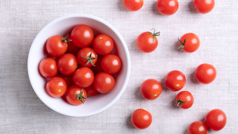 Bowl of fresh red cherry tomatoes in bowl and scattered on counter