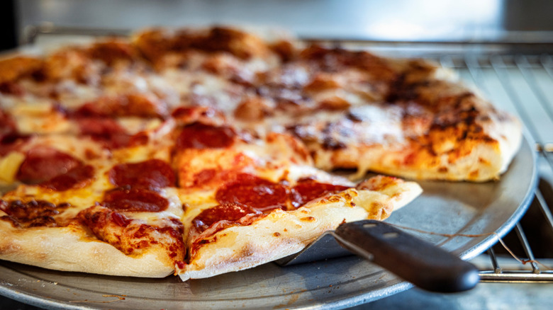 Whole pepperoni pizza on display on a pizza pan with a serving spatula handle visible under one slice