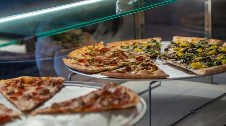 Trays featuring several different slices of pizza on display in a shop