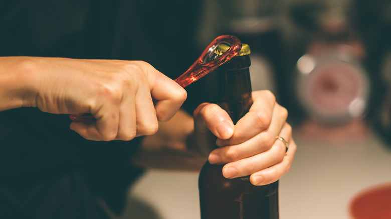 person opening a brown glass bottle of beer