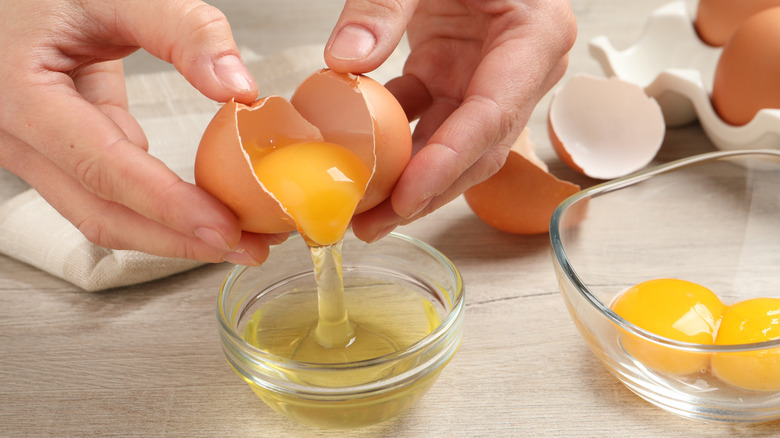 Two hands separating egg over bowl