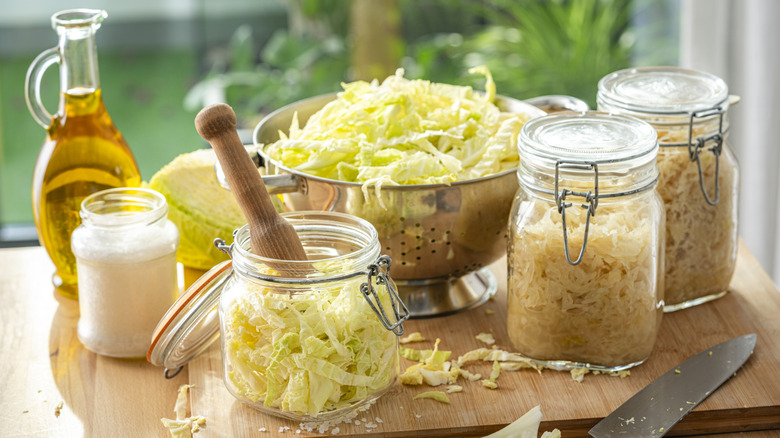 jars of homemade sauerkraut next to bowl of fresh cabbage