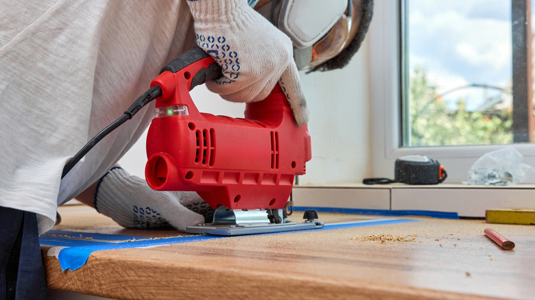 A person cuts a hole for a sink in a custom wooden countertop