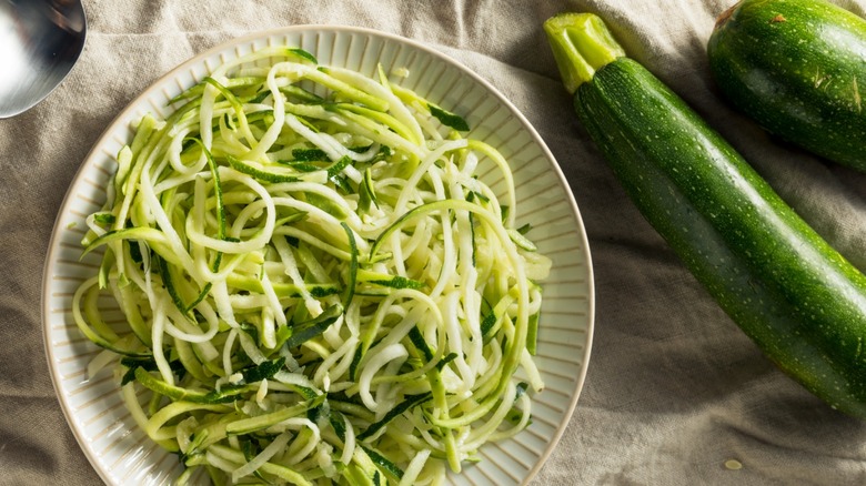Bowl of zoodles next to whole zucchini