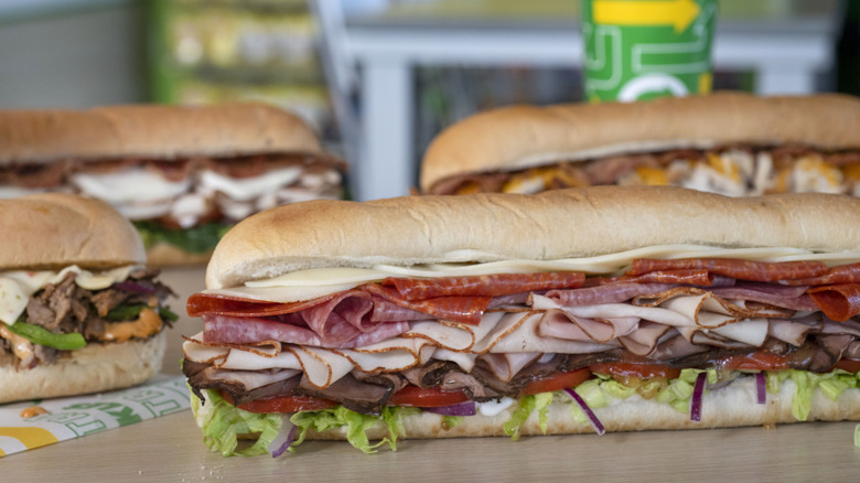 Several Subway sandwiches, with a Subway cup in the background